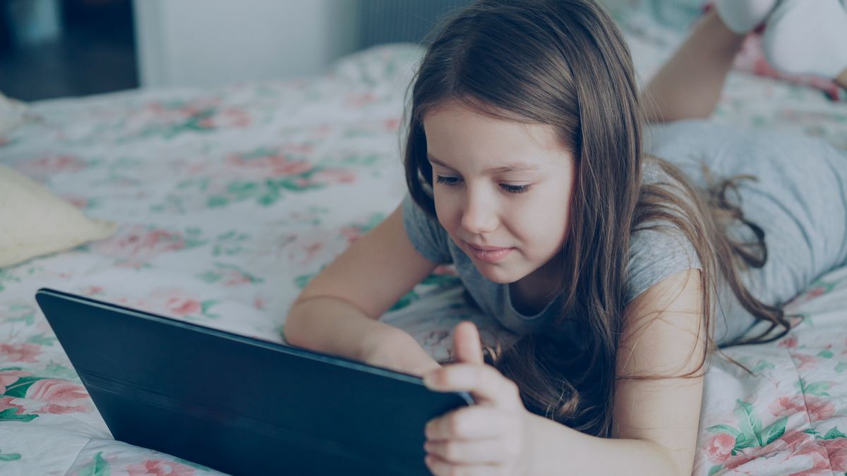Criança usando tablet deitada na cama, ilustrando exposição à luz azul das telas